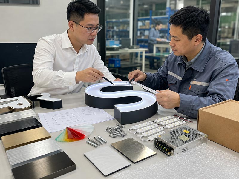 Engineer and salesperson preparing a custom LED sign quote with sign sample, materials, power supply, mounting parts, and color samples