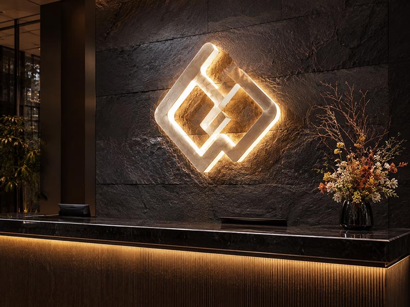 Dual-lit acrylic logo sign with front lighting and soft back halo on a premium wall