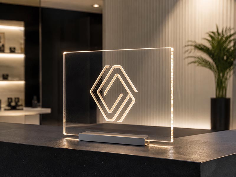 Edge-lit acrylic logo sign with clear glowing acrylic panel on a showroom counter