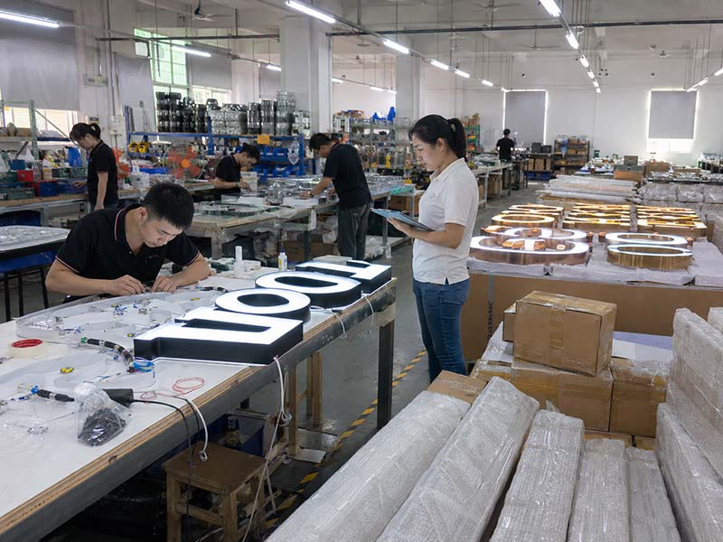 LED sign factory workshop assembling illuminated channel letters with QC inspection and export packing materials for custom signage production.