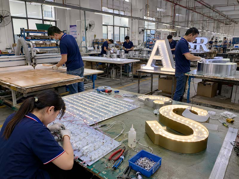 LED sign factory production workshop with workers assembling channel letters and illuminated signage in China