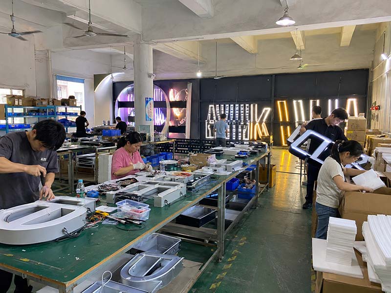 Real LED sign factory workshop with workers assembling, testing, and packing illuminated commercial signs