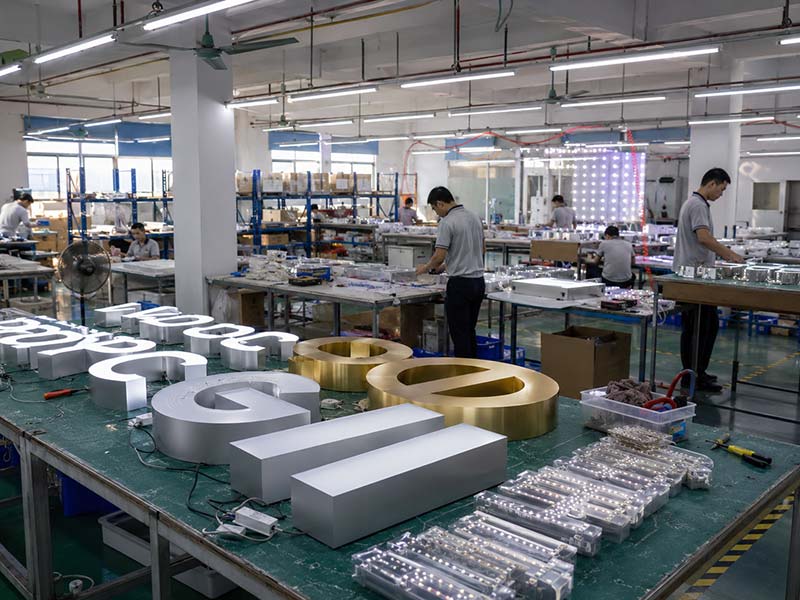 Professional LED sign manufacturing workshop with illuminated channel letters, workers, production tables, and testing areas inside Iduoduo factory.