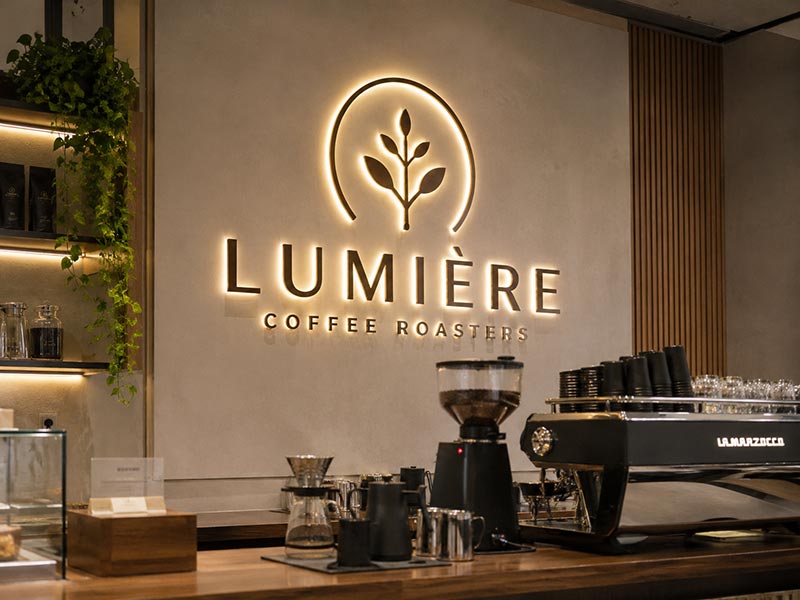 Backlit cafe logo sign with soft halo lighting on an interior brand wall