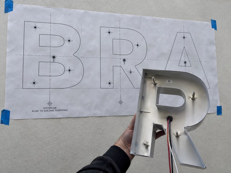 Channel letter mounting pattern showing letter outlines, stud positions, centerlines, and wire exits