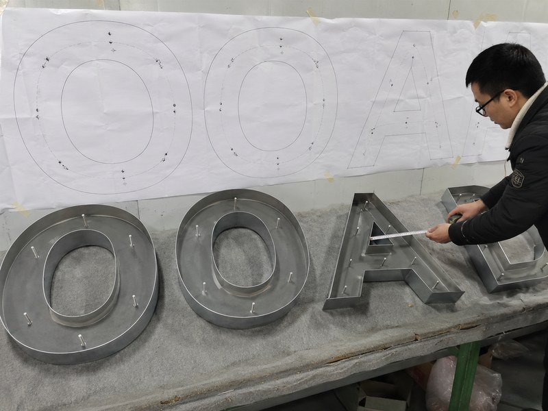Full-size channel letter mounting template checked against the finished letters and stud positions