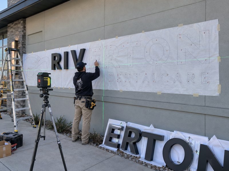 Installer using a full-size template and laser level to position channel letters before mounting