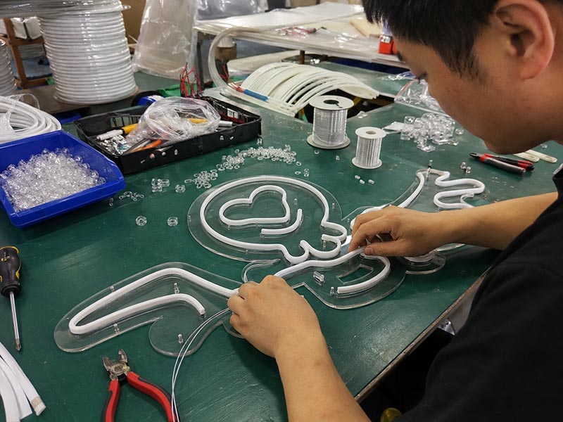 Worker assembling LED neon flex on acrylic backing during custom sign production