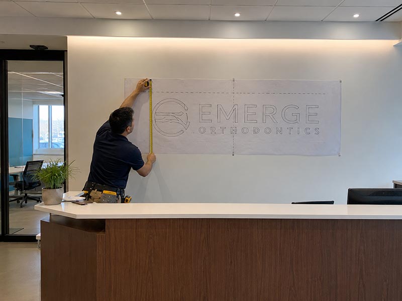 Installer measuring the placement of a reception logo sign behind an office front desk