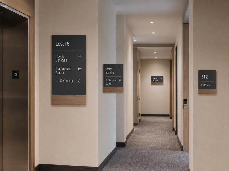 Wayfinding signs placed at an elevator exit corridor junction and room entrance
